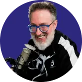 A man with glasses and a beard smiling in front of a microphone.