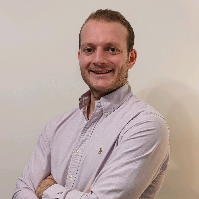 Man in a light shirt smiling at the camera with arms crossed.