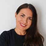 Smiling person with long brown hair wearing a black shirt against a plain background.