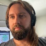 Man with long hair and a beard wearing headphones, looking at a screen.