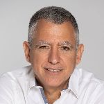 Man with short gray hair wearing a white shirt, smiling at the camera against a gray background.