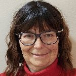 A person with long dark hair and glasses smiles while wearing a red top against a plain background.