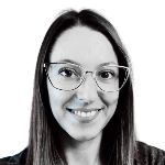A woman with long brown hair and glasses smiles at the camera against a plain white background.