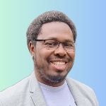 Smiling person with glasses and a beard, wearing a light gray jacket and white shirt, against a blue and green gradient background.