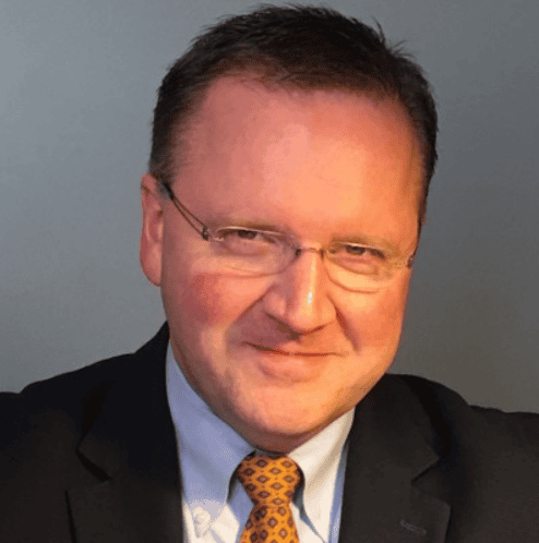 Mike Lyles, a Test Leader in a suit and tie with glasses, is smiling slightly, facing the camera against a plain gray background.
