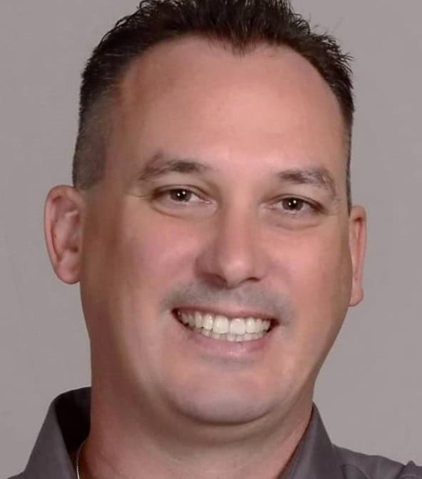 A man with short dark hair smiles at the camera, wearing a gray collared shirt against a plain background, reflecting confidence in DevSecOps and software security.
