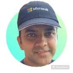 A person wearing a navy blue Microsoft cap is smiling at the camera, with a green and blue circular background. A person wearing a navy blue Microsoft cap is smiling at the camera, with a green and blue circular background.