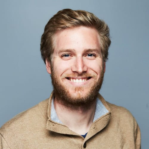 Ben Fellows, a man with blonde hair and a beard, smiles at the camera in a tan pullover sweater against a plain gray background—a welcoming face among top AI Codebase Discovery testers.